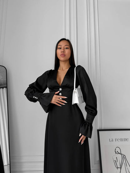 Woman wearing a black dress with a white bag against a gray wall.