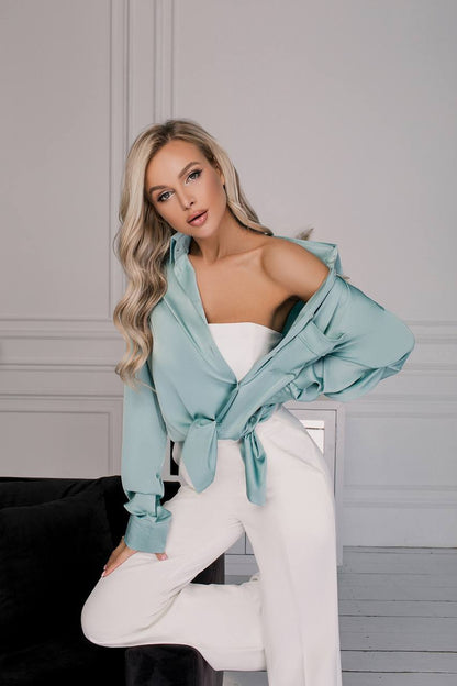 Woman wearing a light blue off-shoulder top and white pants against a neutral background