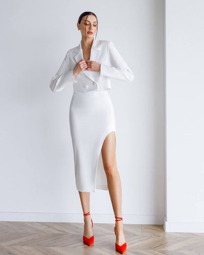 Woman wearing a white outfit with a high slit skirt and red shoes against a plain background