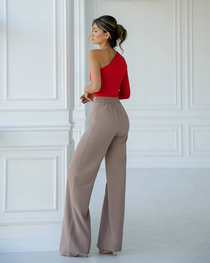 Woman wearing a red top and beige pants against a white paneled wall.