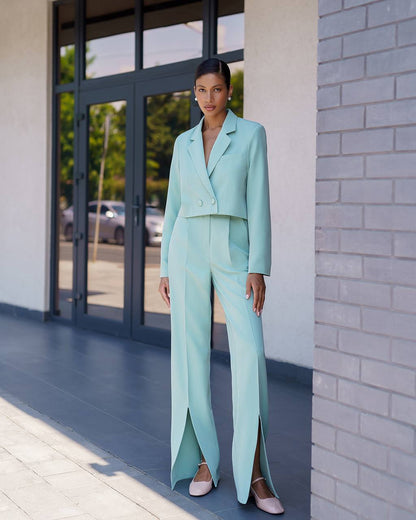 Woman in a light blue suit standing outside a building with glass doors.