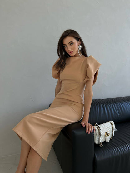 Woman in a beige dress sitting on a black leather couch with a white handbag.