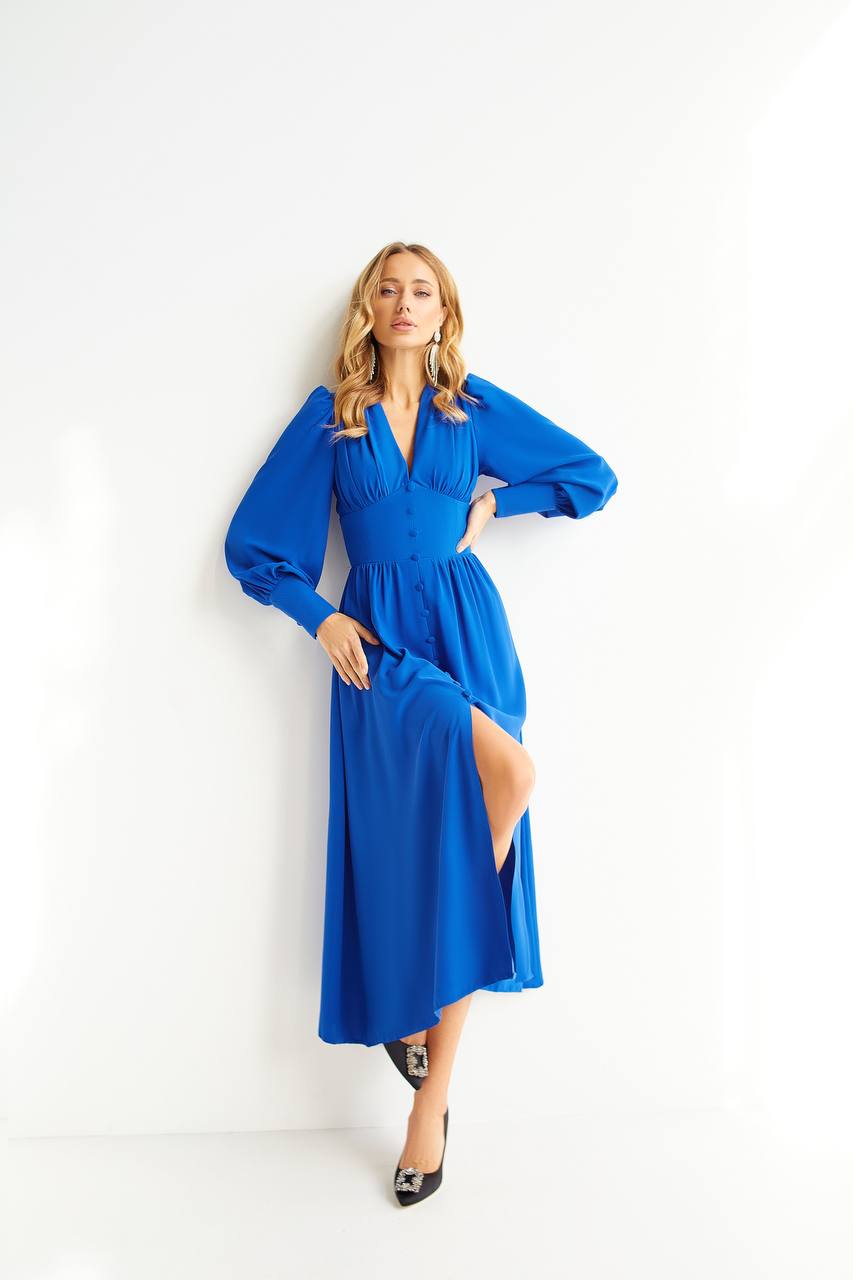 Woman wearing a blue dress with a slit, standing against a white background