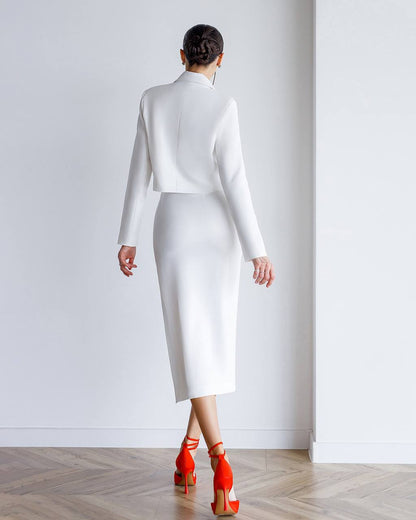 Person wearing a white outfit with red shoes in a minimalistic setting