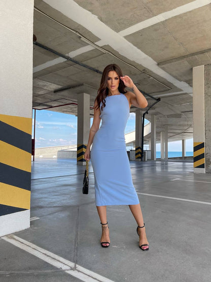 Woman in a light blue dress standing in an industrial setting with concrete pillars and a clear sky.