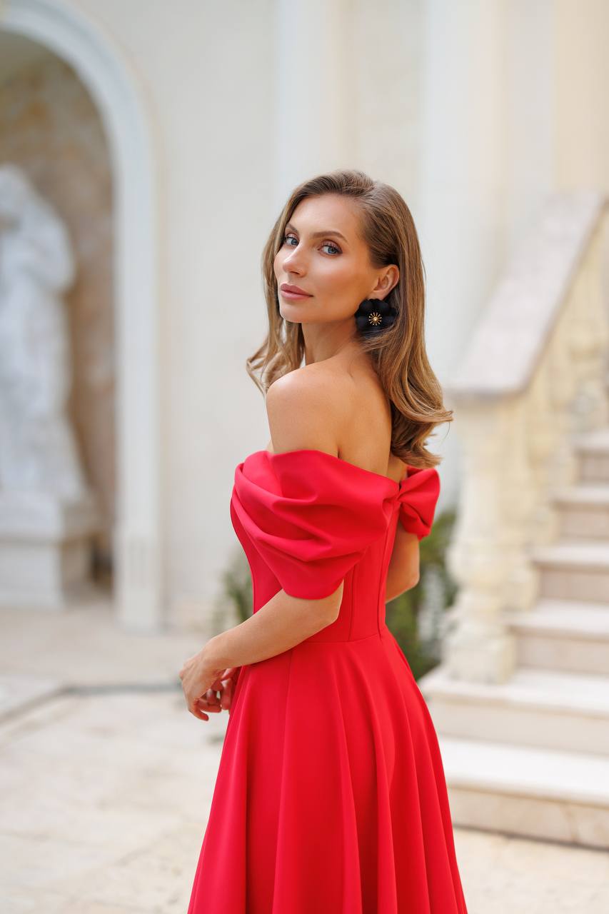 Woman in a red off-shoulder dress standing in an elegant indoor setting.