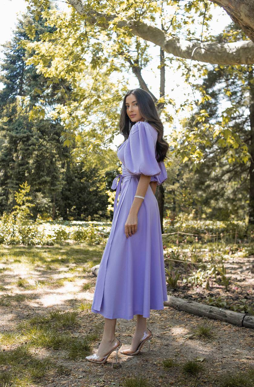 Woman in a purple dress standing in a park with trees and grass in the background