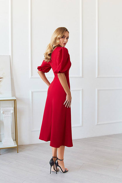 Woman in a red dress standing in a room with white walls and a fireplace.