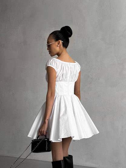 Woman in a white dress holding a black handbag against a gray background