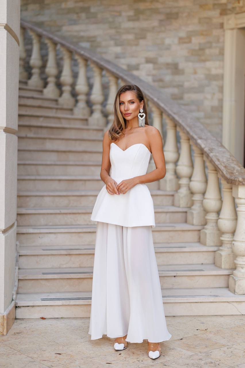 Woman in a white strapless top and wide-leg pants standing on stone steps.