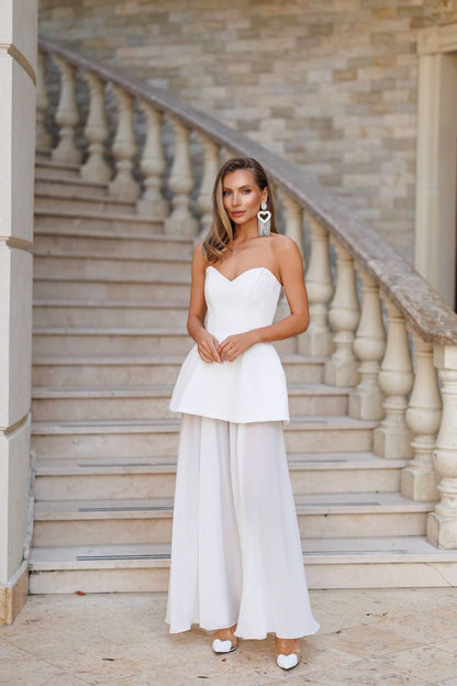 Woman in a white strapless top and wide-leg pants standing on stone steps.