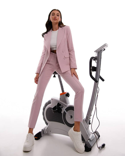Woman in a pink suit standing next to an exercise bike on a white background