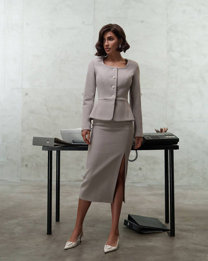 Woman in a gray suit standing next to a desk with a concrete wall background