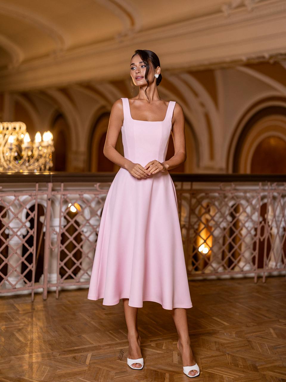 Woman in a pink dress standing in an elegant indoor setting with chandeliers.