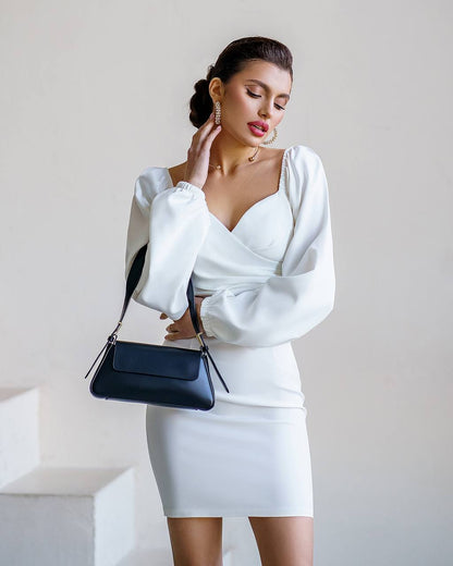Woman in a white outfit holding a blue handbag against a plain background