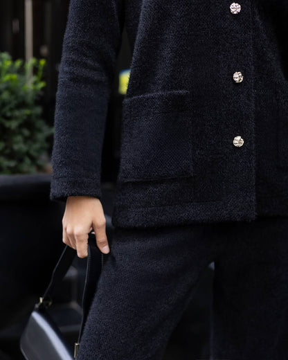 Person wearing a dark coat with buttons, holding a black handbag.