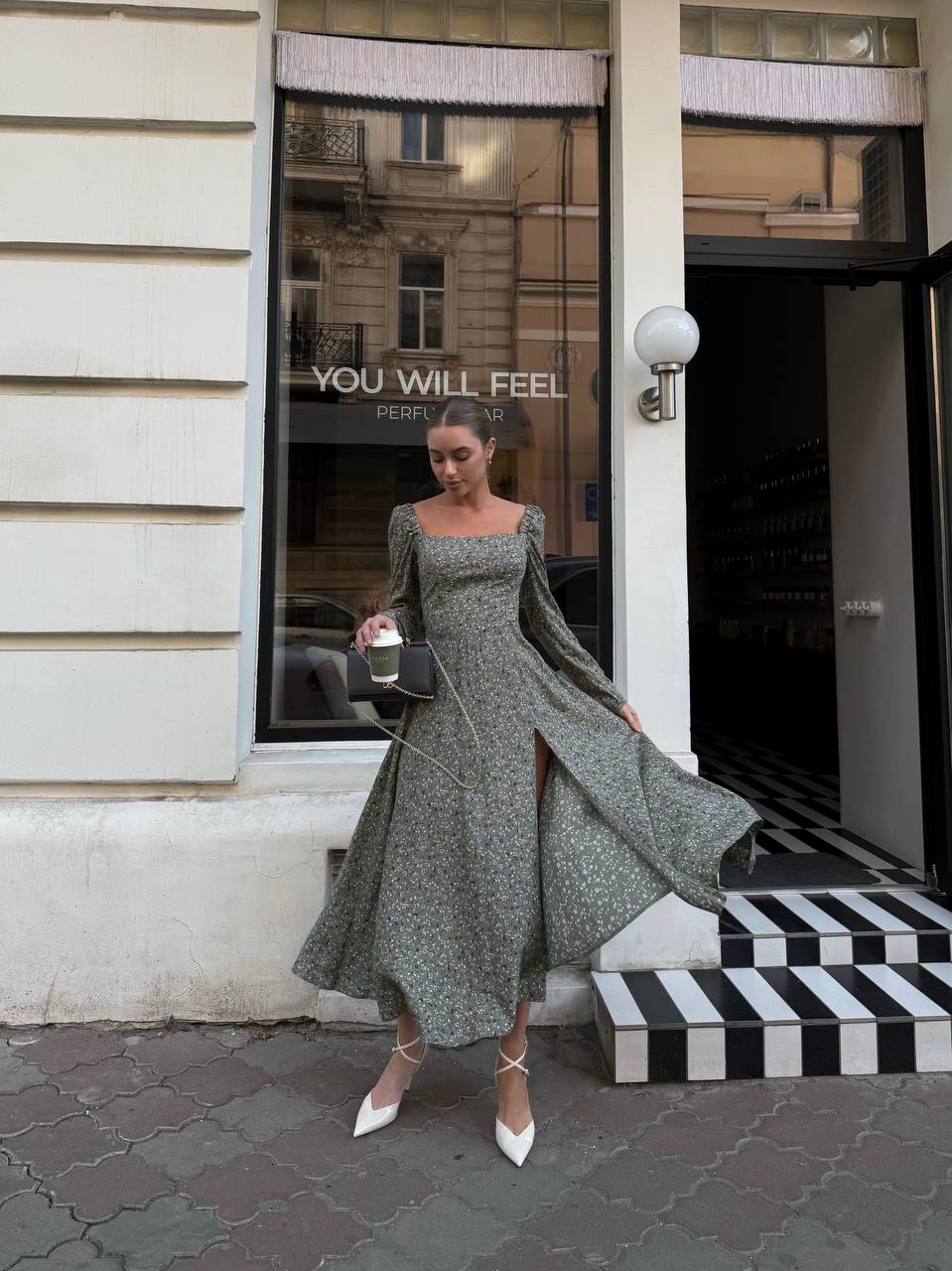 Woman in a long green dress standing outside a store with a reflective window.