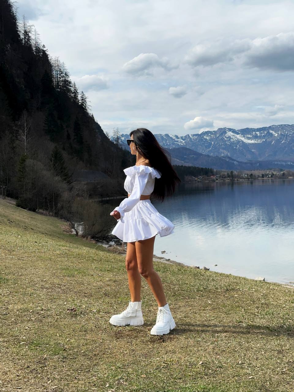 Woman in a white dress standing by a lake with mountains in the background