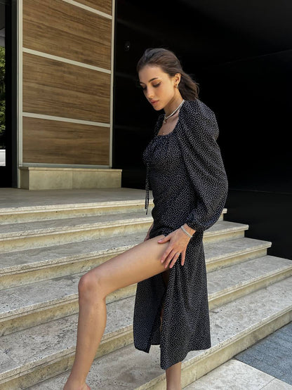 Woman in a black dress standing on steps with a wooden wall background