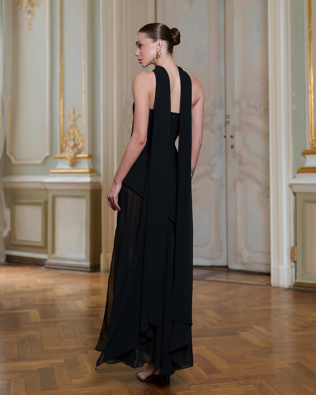 Woman wearing a black dress in an elegant room with decorative walls.