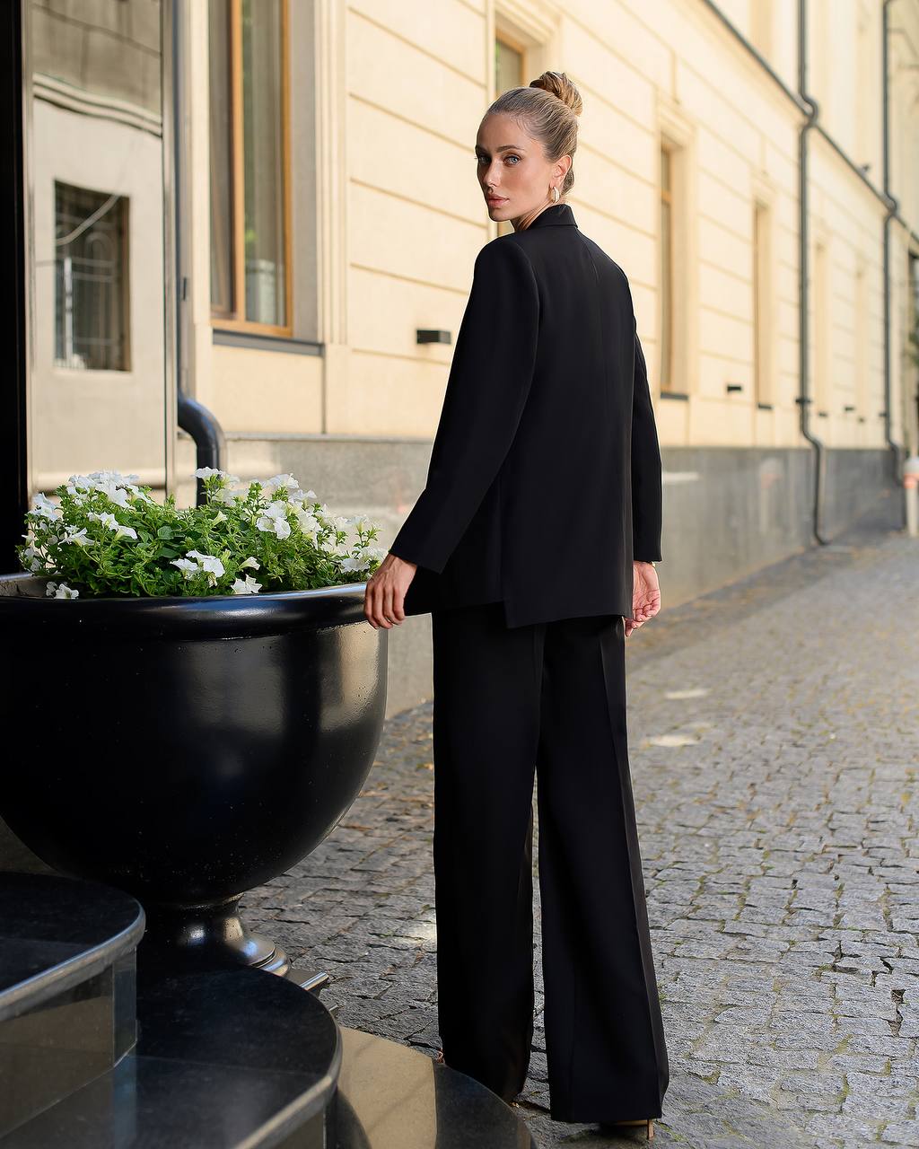 Woman in a black outfit standing on a street with a building and planter in the background