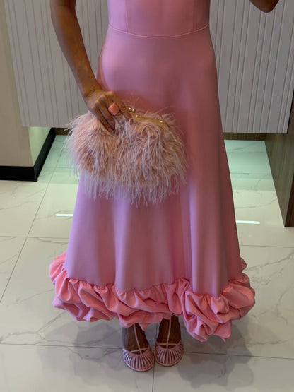 Person wearing a pink dress with ruffles holding a feathered clutch.