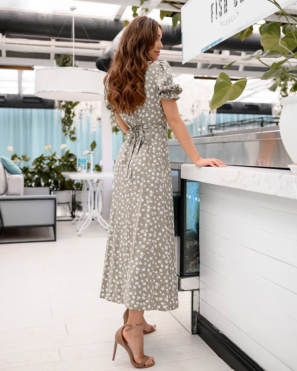 Woman in a patterned dress standing by a counter in a modern indoor setting with plants.