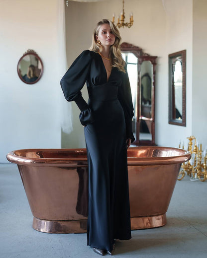 Woman in a black dress standing next to a copper bathtub in an elegant room.