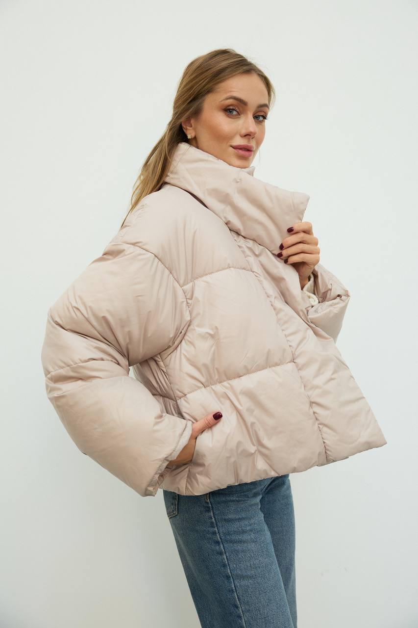 Woman wearing a beige puffer jacket against a white background
