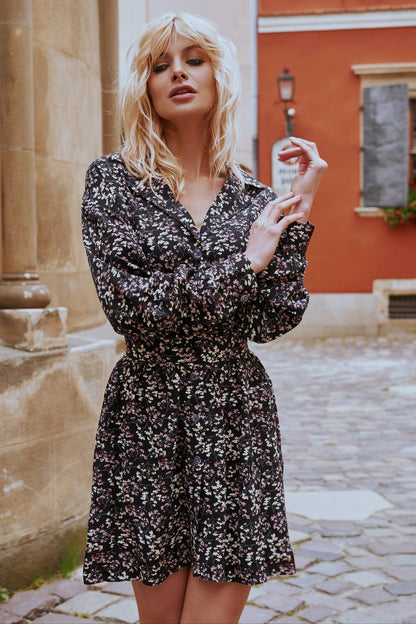 Woman in a floral dress standing on a cobblestone street with a building in the background