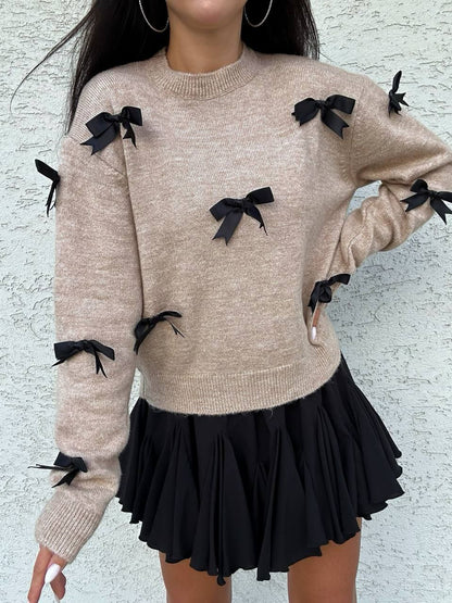 Beige sweater with black bows and a black skirt on a light gray background