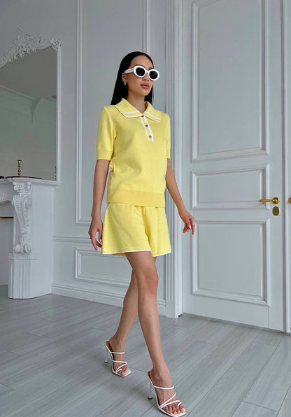 Woman in a yellow outfit standing in a stylish room with white walls and a door.