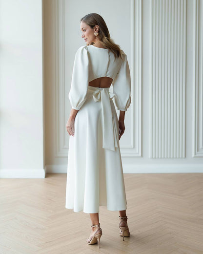 Woman wearing a white outfit with cut-out design in a room with wooden floor and white walls.
