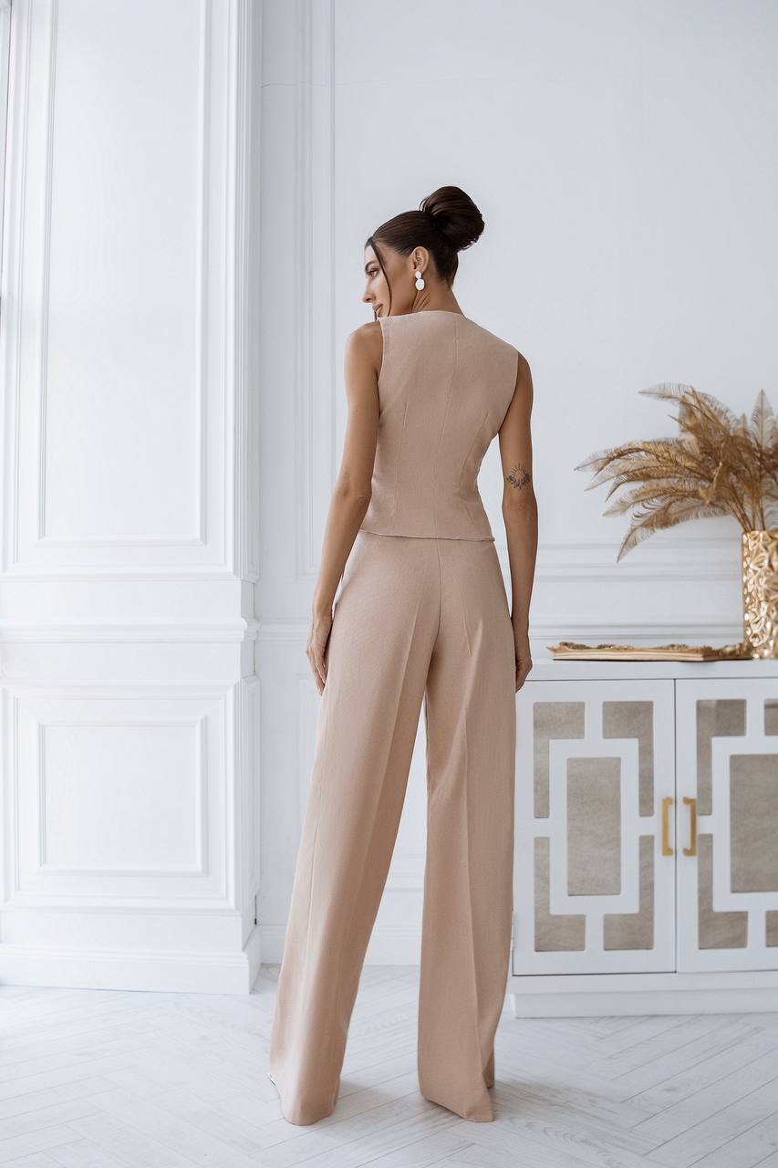 Woman wearing a beige jumpsuit in a stylish room with decorative elements.