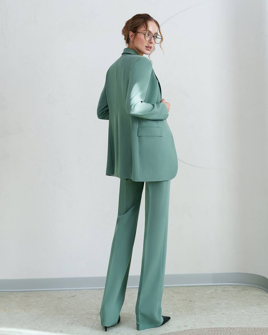 Person wearing a green suit standing against a plain white wall.
