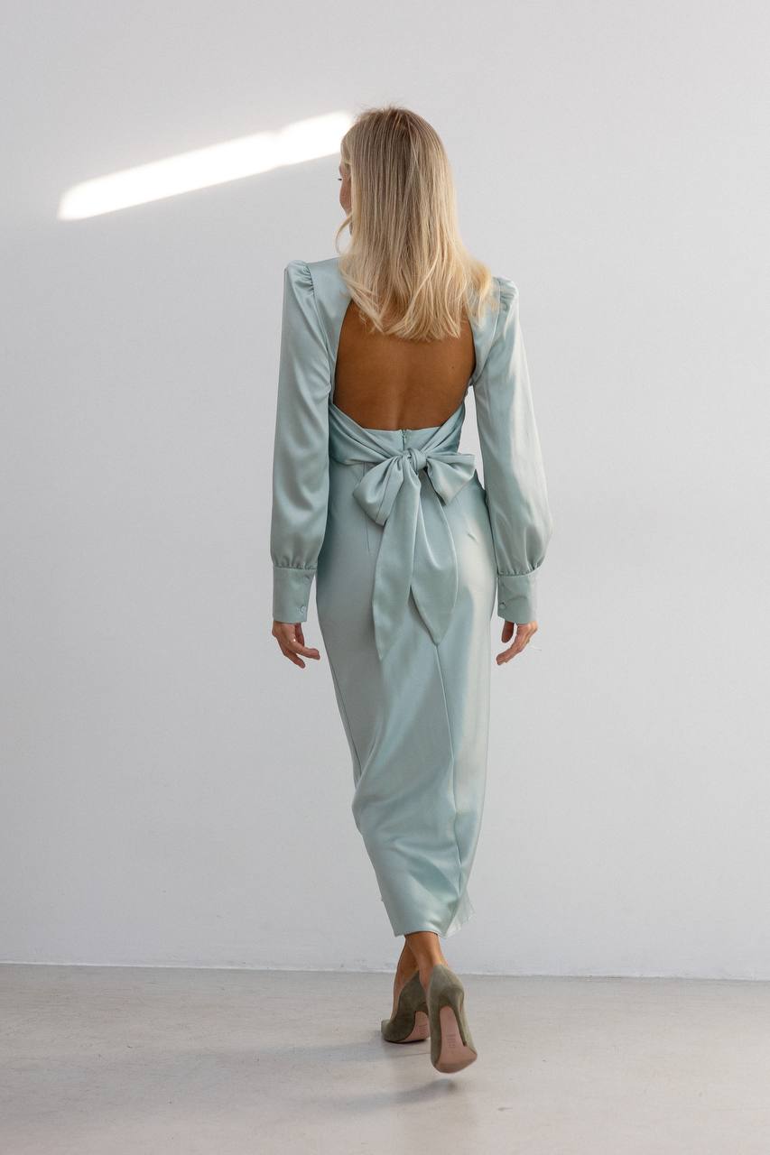 Woman wearing a light blue satin dress with a bow detail, standing against a white background.