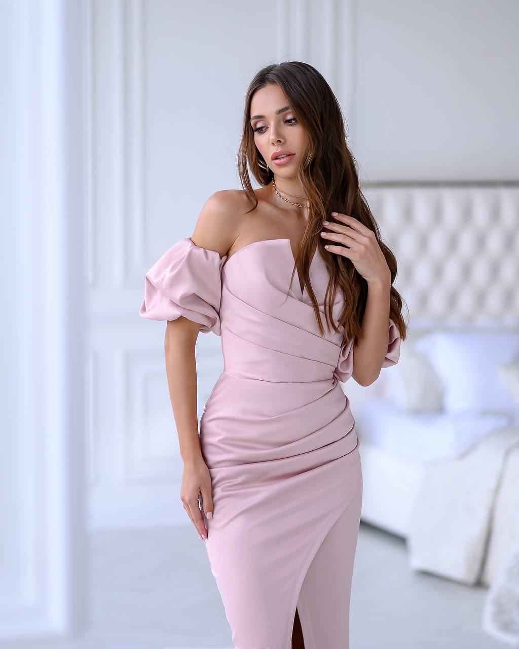Woman wearing a pink off-shoulder dress in a room with white decor.