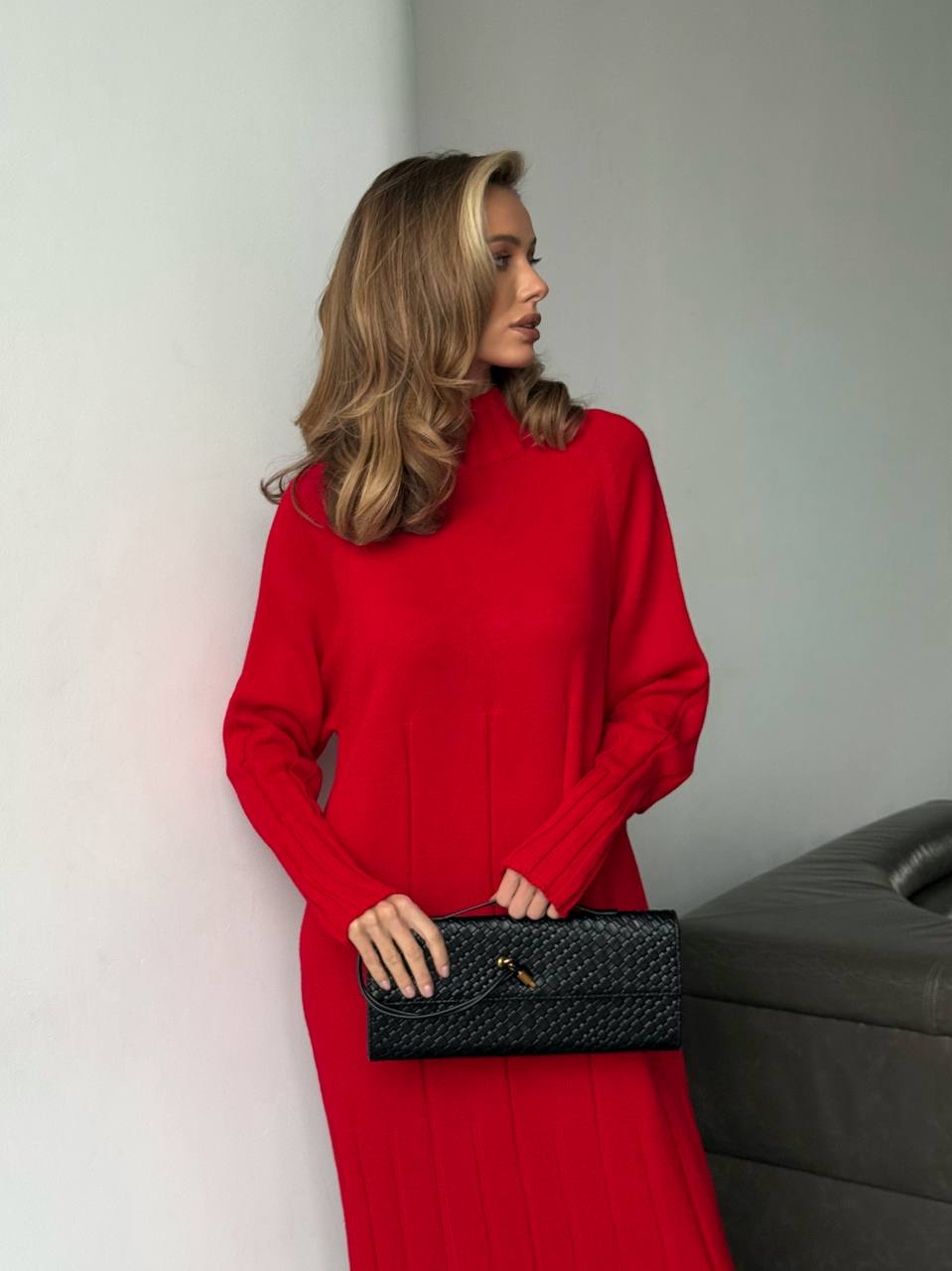 Woman in a red dress holding a black clutch against a neutral background