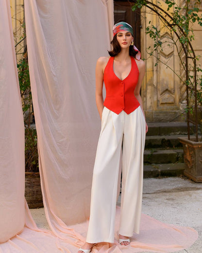 Woman in a red top and white pants standing in front of a draped curtain.