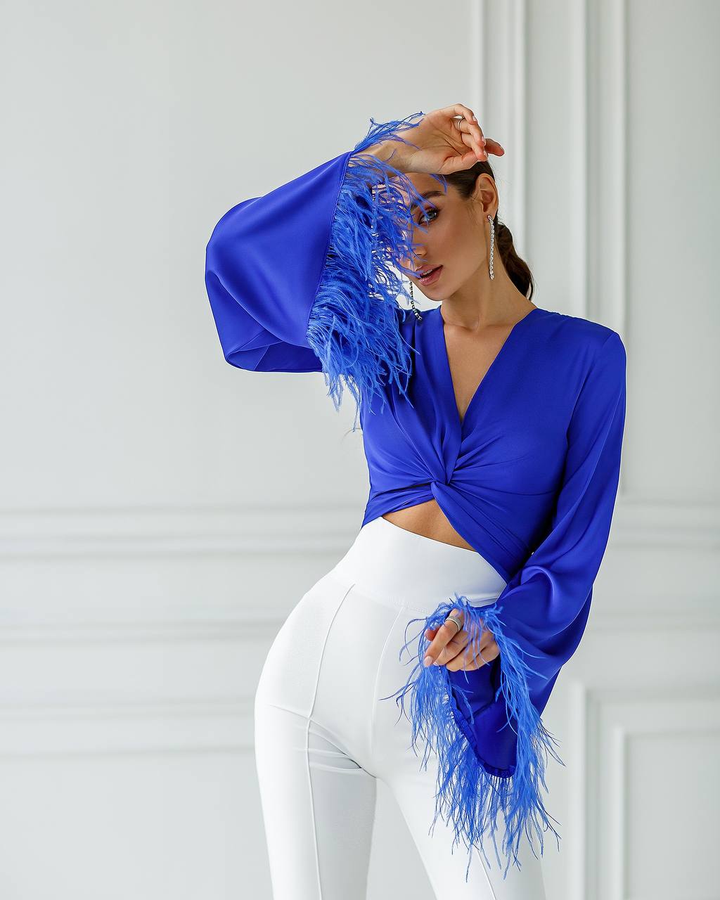 Woman wearing a blue top with feathered sleeves against a white wall