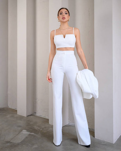 Woman in a white outfit holding a white hat against a plain background