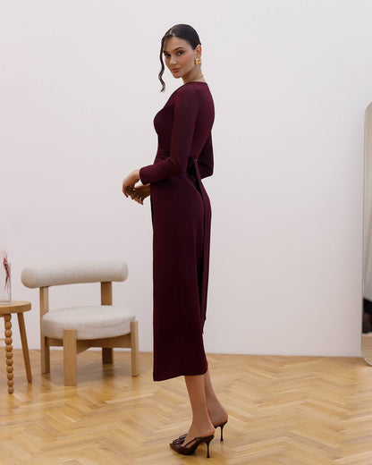 Woman in a burgundy dress standing in a room with wooden flooring and a white wall.