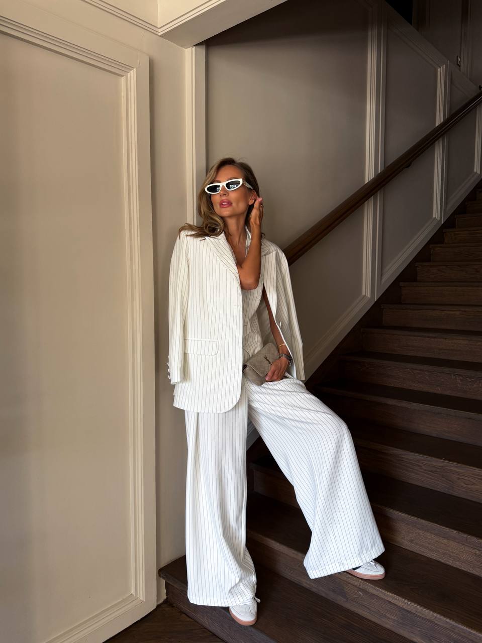 Woman in a white outfit standing on a staircase with wainscoted walls.