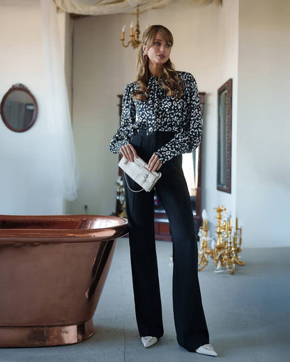 Woman in a patterned blouse and black pants standing in an elegant room with a copper bathtub.
