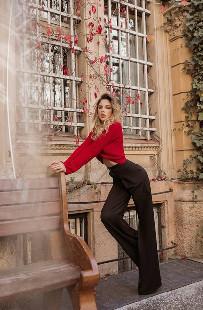 Woman in a red top and black pants standing in front of a decorative window.