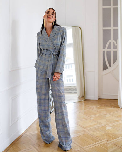 Woman wearing a blue plaid suit standing in a room with white walls and wooden floor.