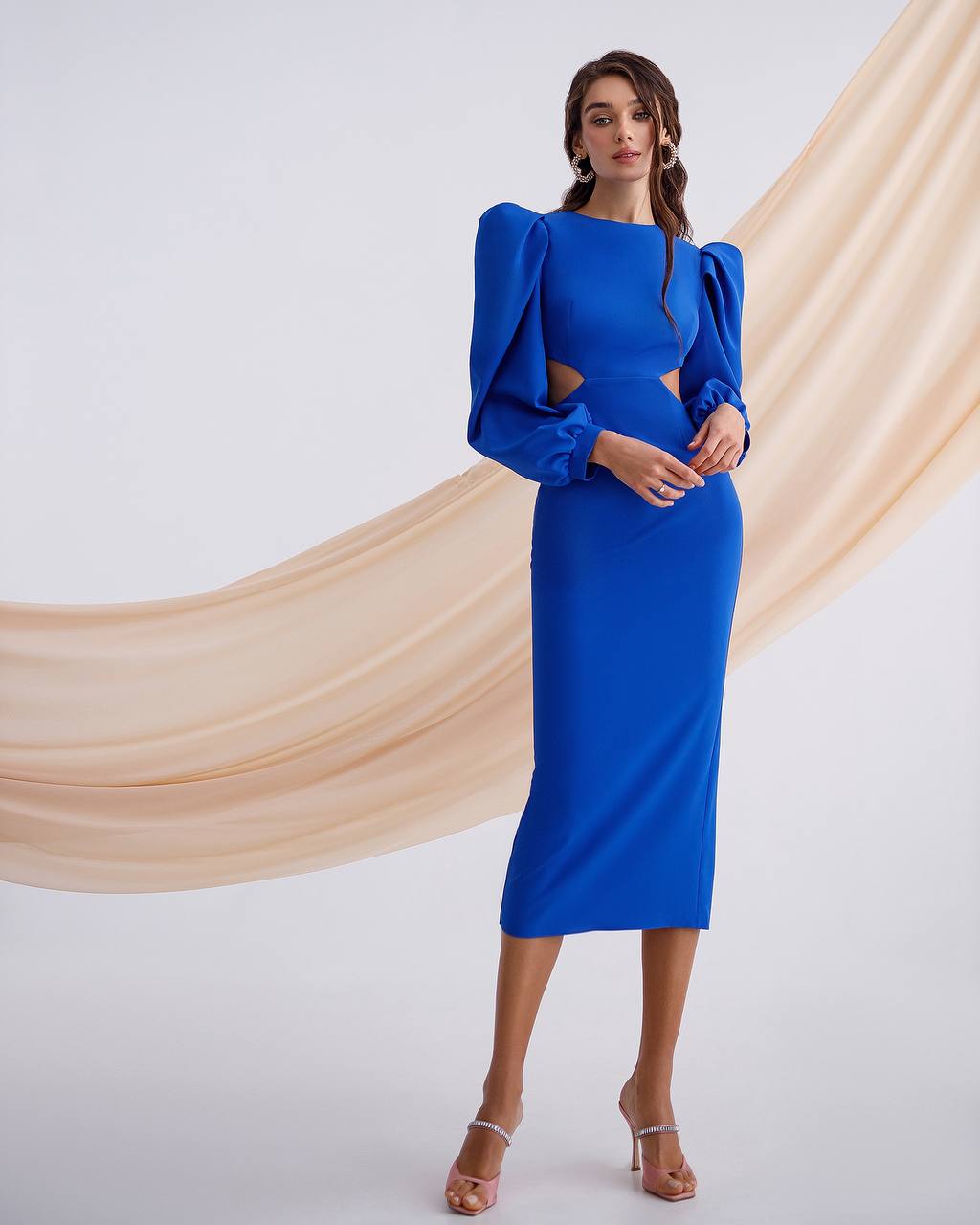 Woman wearing a blue dress with cut-out design against a beige curtain backdrop