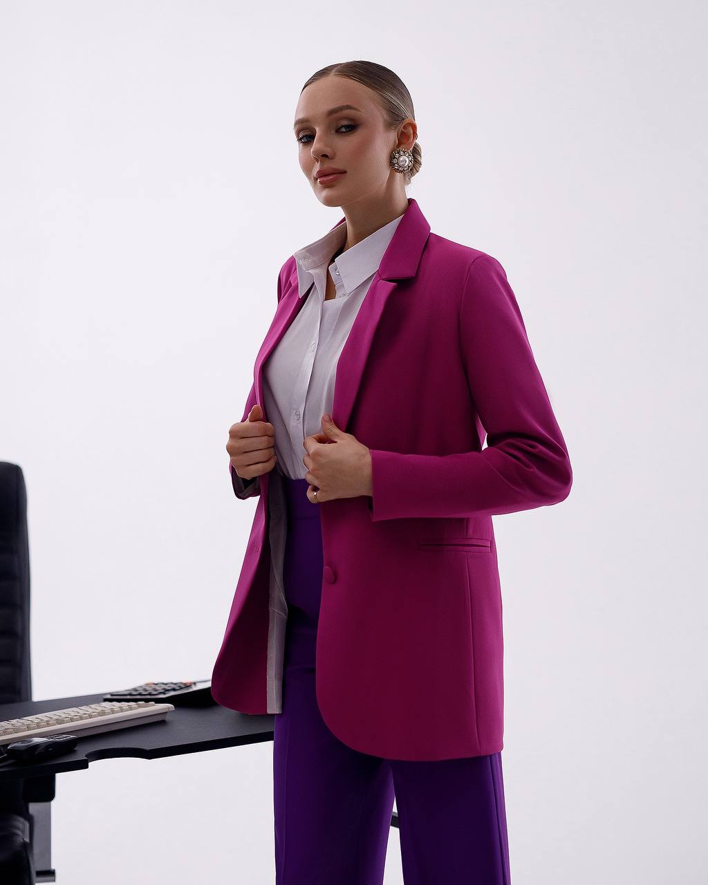 Person wearing a bright pink blazer over a white shirt with purple pants on a white background