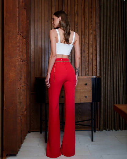 Woman wearing a white top and red pants standing in a room with wooden walls and furniture.