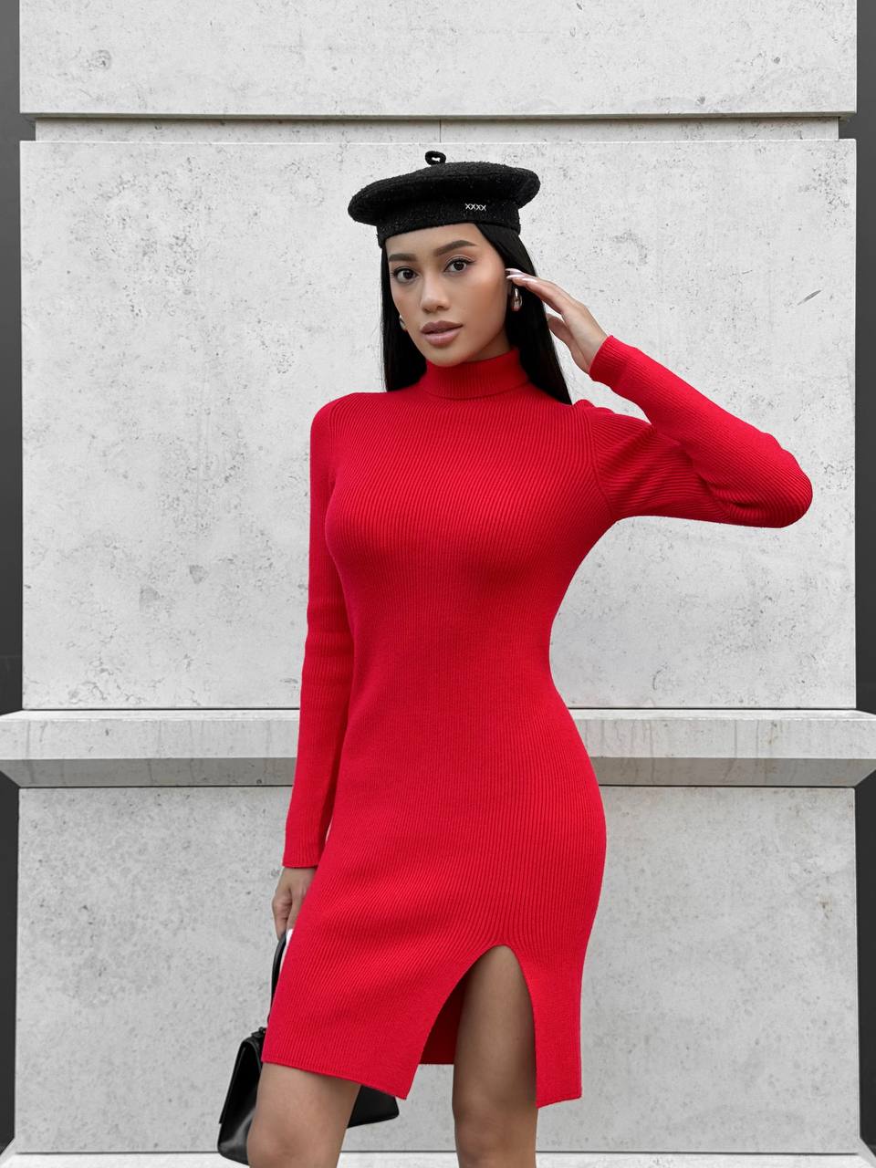 Woman wearing a red dress and black beret against a light gray wall.